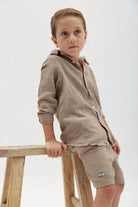 Kids' Tetra Set - Mocha. A young boy in a mocha-colored textured shirt and shorts with an eye emblem on the shorts