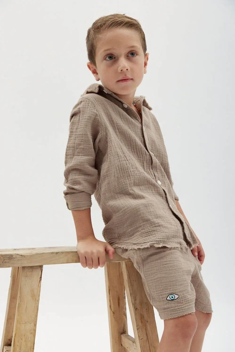 Kids' Tetra Set - Mocha. A young boy in a mocha-colored textured shirt and shorts with an eye emblem on the shorts