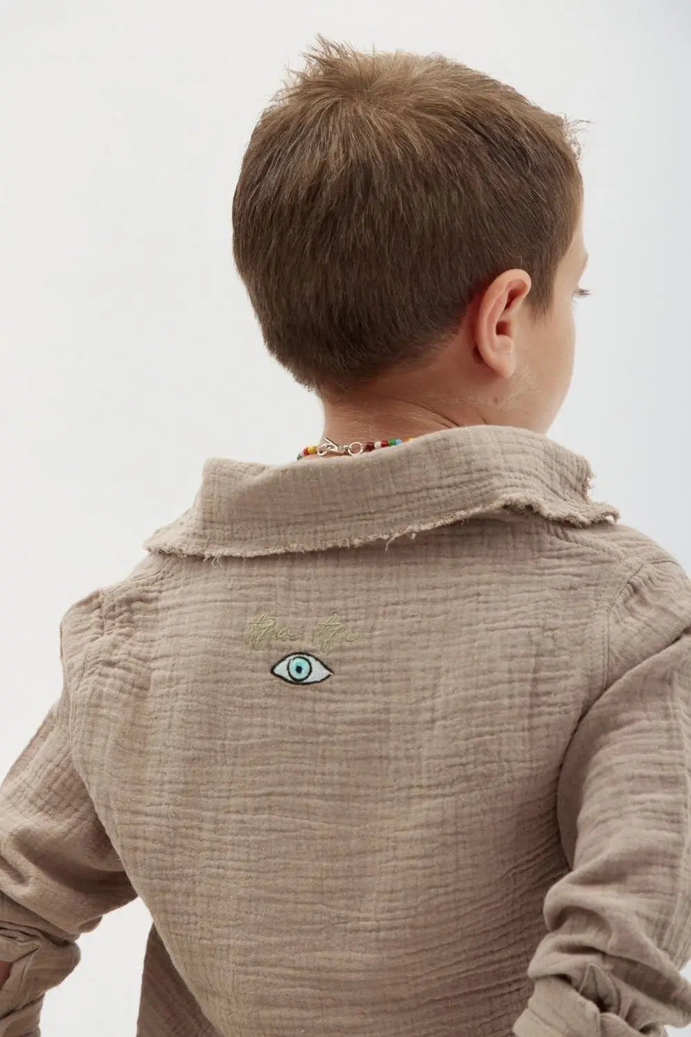 Back of a child wearing the Kids' Tetra Set - Mocha, showing an embroidered eye design and text on the back of the shirt
