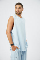 Man wearing a light blue sleeveless shirt and light blue pants on a white background