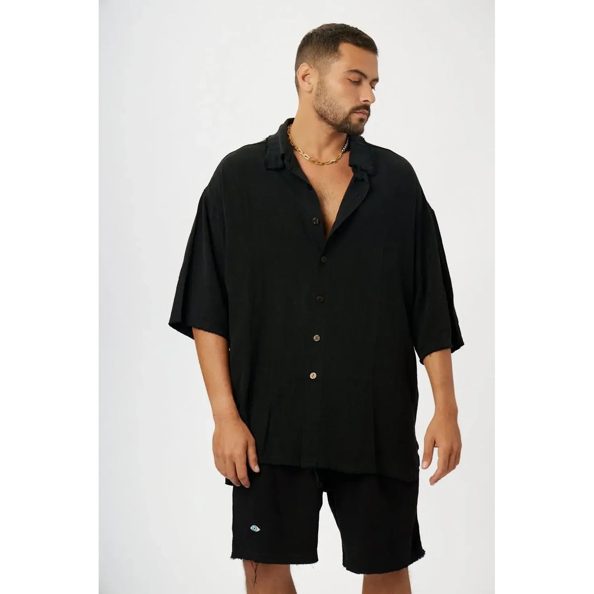 Man wearing a black soft linen short sleeve button-up shirt and black shorts