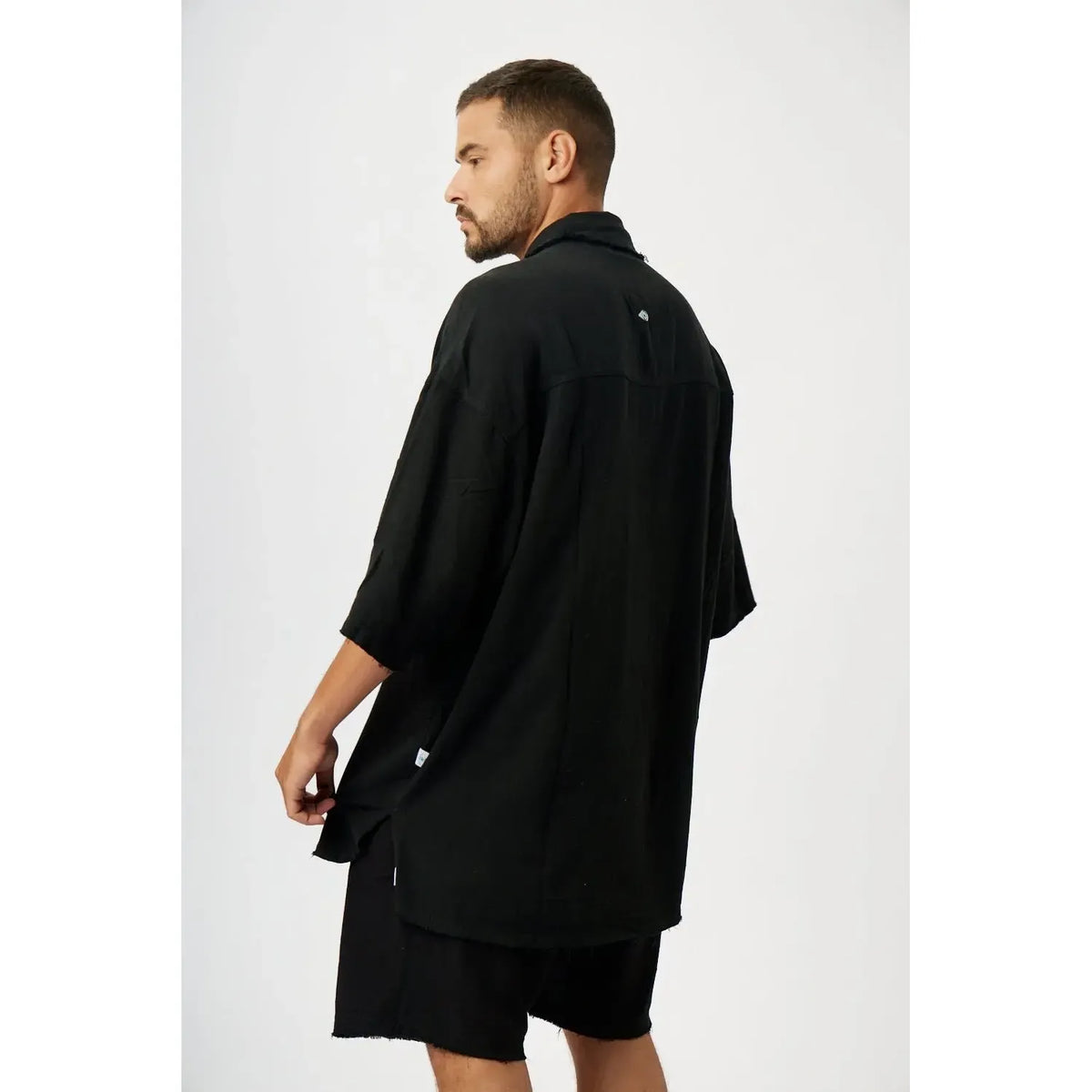 Man wearing a black Soft Linen Short Sleeve Button-Up Shirt and black shorts, viewed from behind
