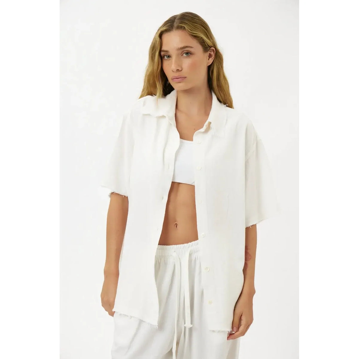 Woman wearing a white Soft Linen Short Sleeve Button-Up Shirt, unbuttoned over a white bralette and white linen shorts