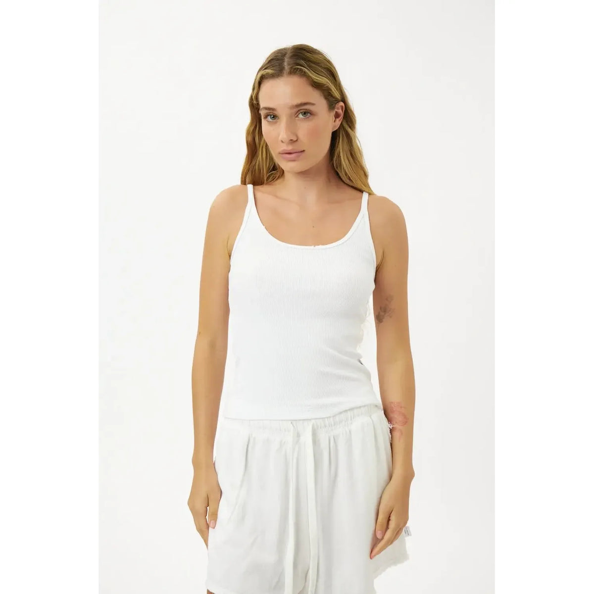 Woman wearing a white tank top and white pants on a white background