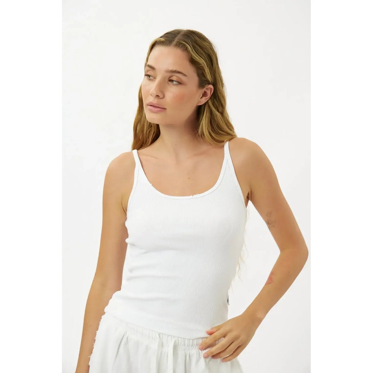 Woman wearing a white tank top against a plain background