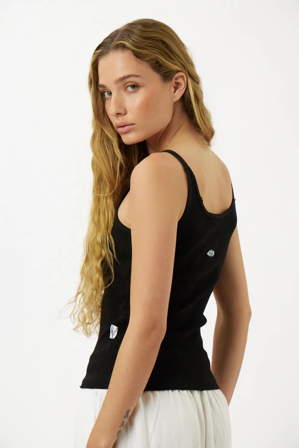 Slim Cotton Tank Top in black, worn by a woman with long blonde hair, looking over her shoulder