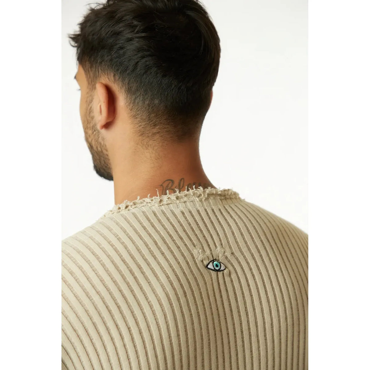 Back of a man wearing a stone striped knit shirt with an eye graphic