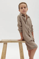 Young boy wearing a Kids' Tetra Set in Mocha, leaning on a wooden stool