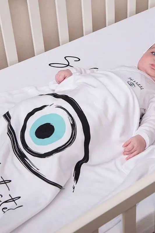 Baby in a crib wearing a white Cotton Single Elliptical Eye Blanket with a large blue and black eye design