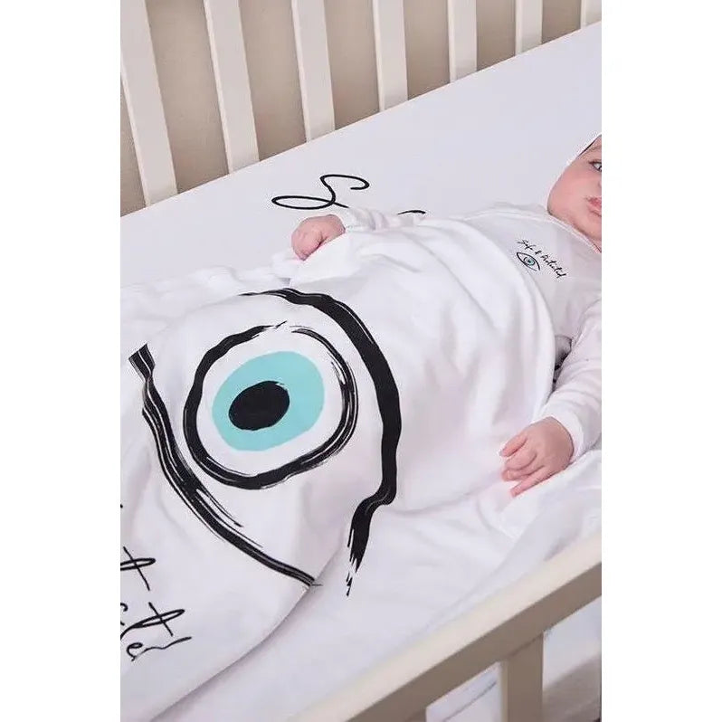 Baby in a crib wearing a white Cotton Single Elliptical Eye Blanket with a large blue and black eye design