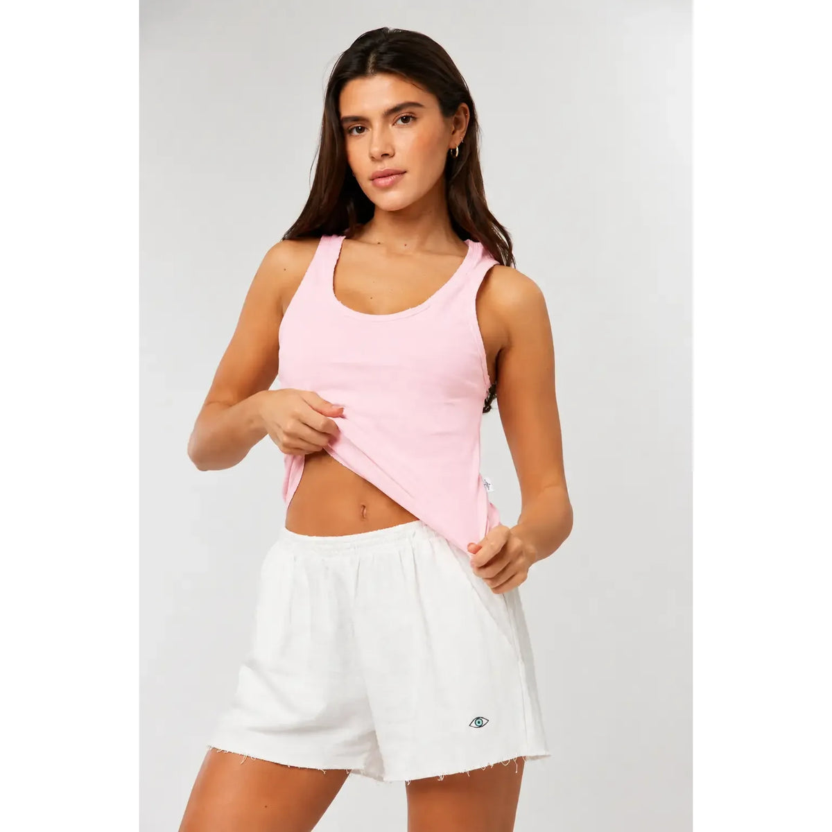 Woman wearing a pink tank top and white shorts on a plain background